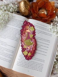 This fantasy autumnal fall sleeping dragon elixir bookmark features a little green dragon curled up in a potion bottle with their tale sticking out the top. Surrounded by orange, green, and light pink foliage with little stars and magic bubbles floating around. On a maroon background