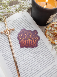 BURN Spark of The Everflame Vinyl Sticker from the Kindred's Curse Saga by Penn Cole. This licensed sticker is maroon with flames and BURN in big letters, with the colors looking like flames, little embers flying around.