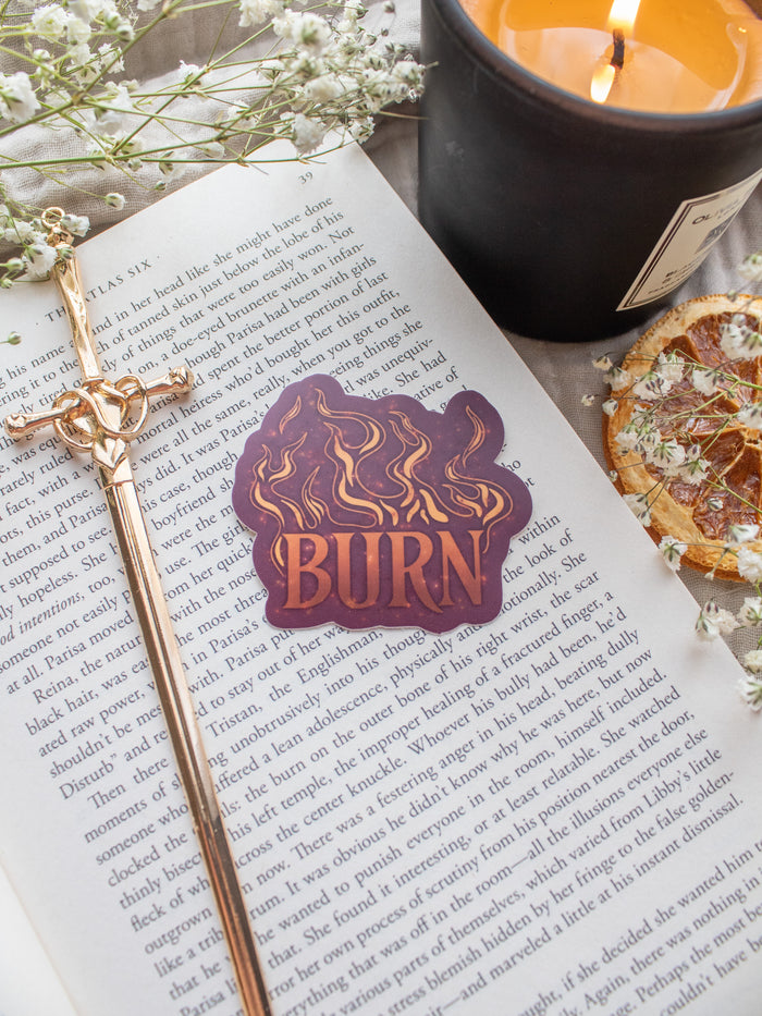 BURN Spark of The Everflame Vinyl Sticker from the Kindred's Curse Saga by Penn Cole. This licensed sticker is maroon with flames and BURN in big letters, with the colors looking like flames, little embers flying around.