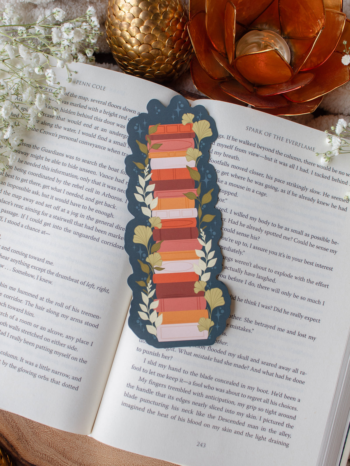 This moody toned fall autumn bookstack bookmark is a bookstack in warm tones, like mustard yellow, cream, coral, and burnt orange on a deep teal background.