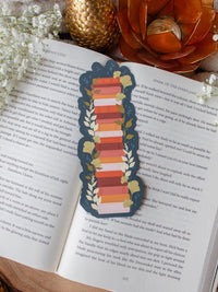 This moody toned fall autumn bookstack bookmark is a bookstack in warm tones, like mustard yellow, cream, coral, and burnt orange on a deep teal background.