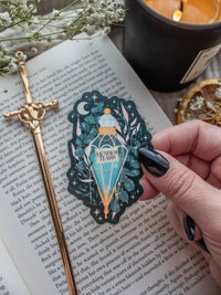 Spark Of The Everflame Henri's Tears Potion Sticker from the Kindred's Curse Saga by Penn Cole. This officially licensed sticker has a dark teal background, with a diamond shaped potion, light teal contents, surrounded by various shades of teal and pink foliage, stars, a crescent moon, and lil magical bubbles.