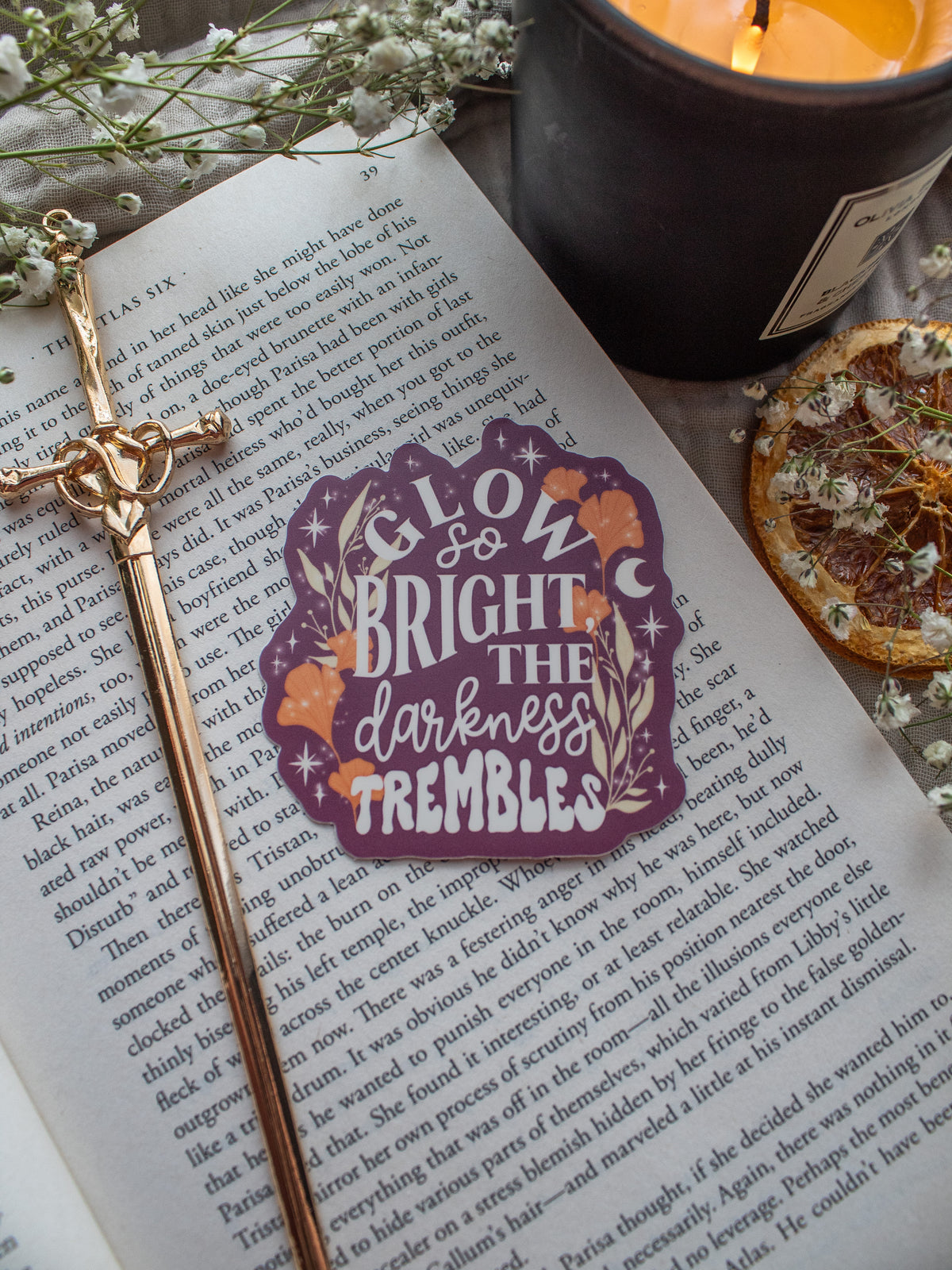 Maroon Sticker with the text "low So Bright The Darkness Trembles" from Spark of the Everflame by Penn Cole from the Kindred's Curse Saga. The text on this officially licensed sticker is surrounded by orange and tan foliage, stars, and magical looking bubbles.