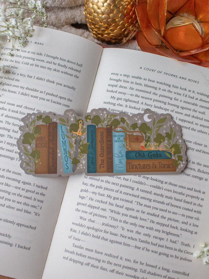 Inspired by Spark of the Everflame from the Kindreds Curse Sage by Penn Cole, this officially licensed Diem's bookshelf bookmark features a bookshelf in earth tones, dark teal blue and light sky blue. The books have titles like "The Guardians", Old Gods, Mortal Medicine and other nods at the series. Surrounded by foliage, the Sword of Corbois, a Lumnos healers clinic satchel, a moon shaped flameroot bottle, and Diem's Lunmos crown.