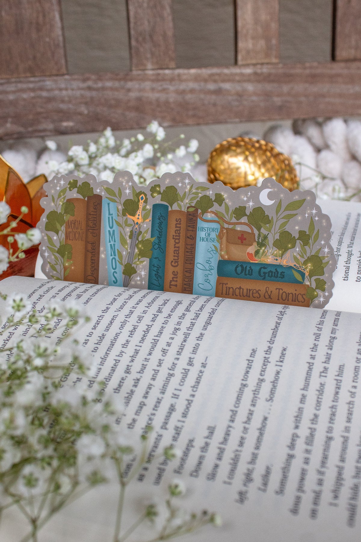 Inspired by Spark of the Everflame from the Kindreds Curse Sage by Penn Cole, this officially licensed Diem's bookshelf bookmark features a bookshelf in earth tones, dark teal blue and light sky blue. The books have titles like "The Guardians", Old Gods, Mortal Medicine and other nods at the series. Surrounded by foliage, the Sword of Corbois, a Lumnos healers clinic satchel, a moon shaped flameroot bottle, and Diem's Lunmos crown.