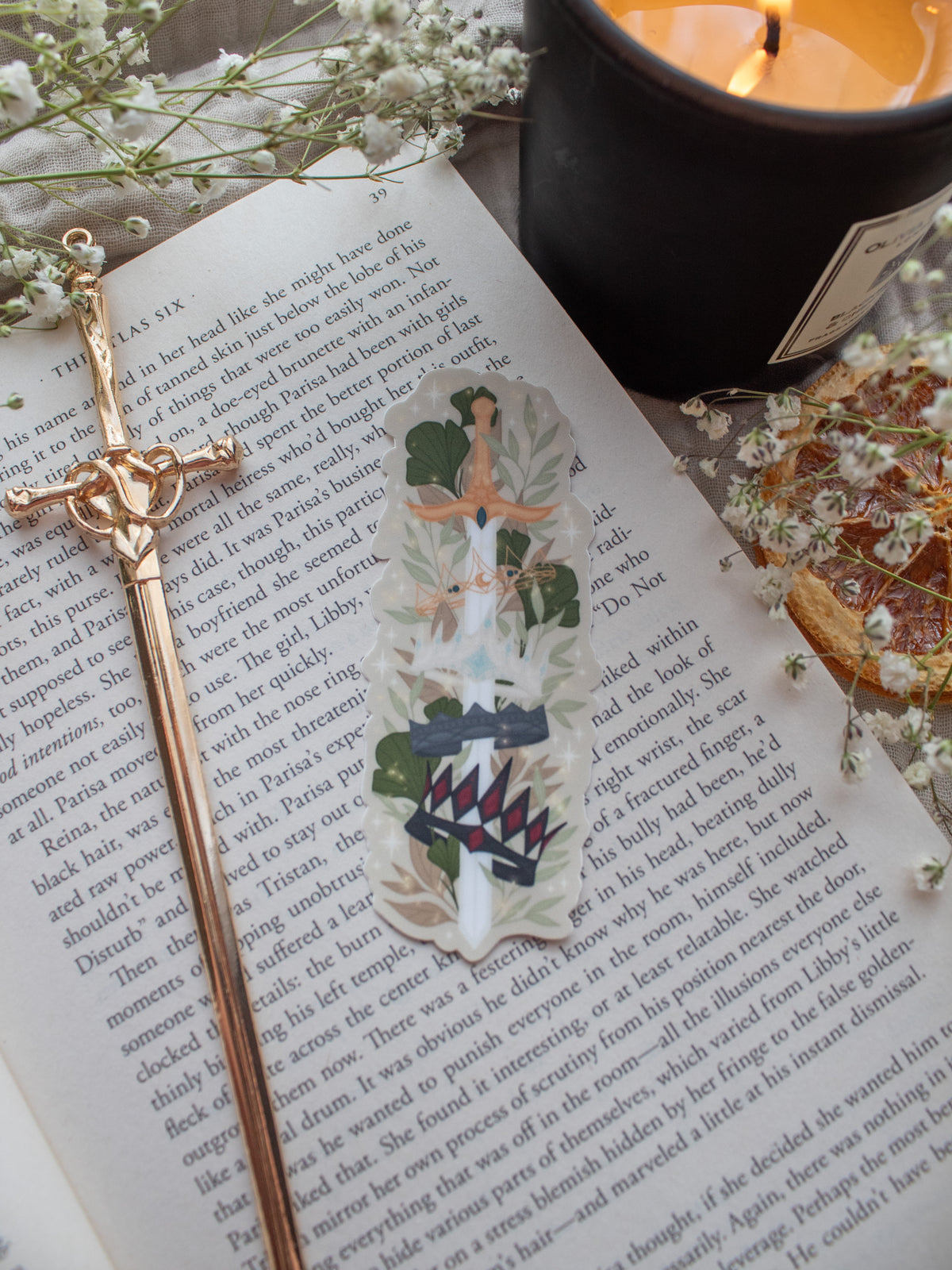 Spark of The Everflame Diem's Crown Sword Sticker, Lunmos Crown, Montios Crown, Fortos Crown, Umbros Crown. From The Kindred's Curse Saga by Penn Cole. This officially licensed sticker is a sword on a light tan background, through the forementioned crowns. Surrounded by foliage.