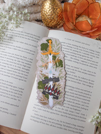 Inspired by Spark of the Everflame from the Kindreds Curse Saga by Penn Cole, this Crown Sword bookmark showcases crowns from four Emarion's realms. *Spoiler Alert, through Heat of the Everflame* - It shows all four crowns Diem has by the end of the 3rd book - Lumnos, Montios, Fortos, and Umbros.  All around a sword that is through the center of them, stacked one on top of the other. On a light beige background and surrounded by foliage, stars and lil magic light bubbles.