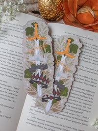 Inspired by Spark of the Everflame from the Kindreds Curse Saga by Penn Cole, this Crown Sword bookmark showcases crowns from four Emarion's realms. *Spoiler Alert, through Heat of the Everflame* - It shows all four crowns Diem has by the end of the 3rd book - Lumnos, Montios, Fortos, and Umbros.  All around a sword that is through the center of them, stacked one on top of the other. On a light beige background and surrounded by foliage, stars and lil magic light bubbles.