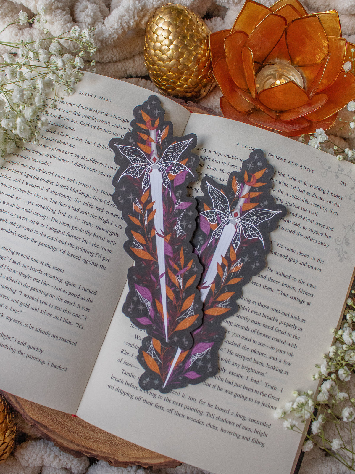 This spooky Halloween Haunted Faerie Dagger dagger bookmark is a long silver dagger with whispy faerie wings that look like spiderwebs. Surrounded but orange, green and maroon foliage covered in spiderwebs. Little stars and magic bubbles all around. Black background.