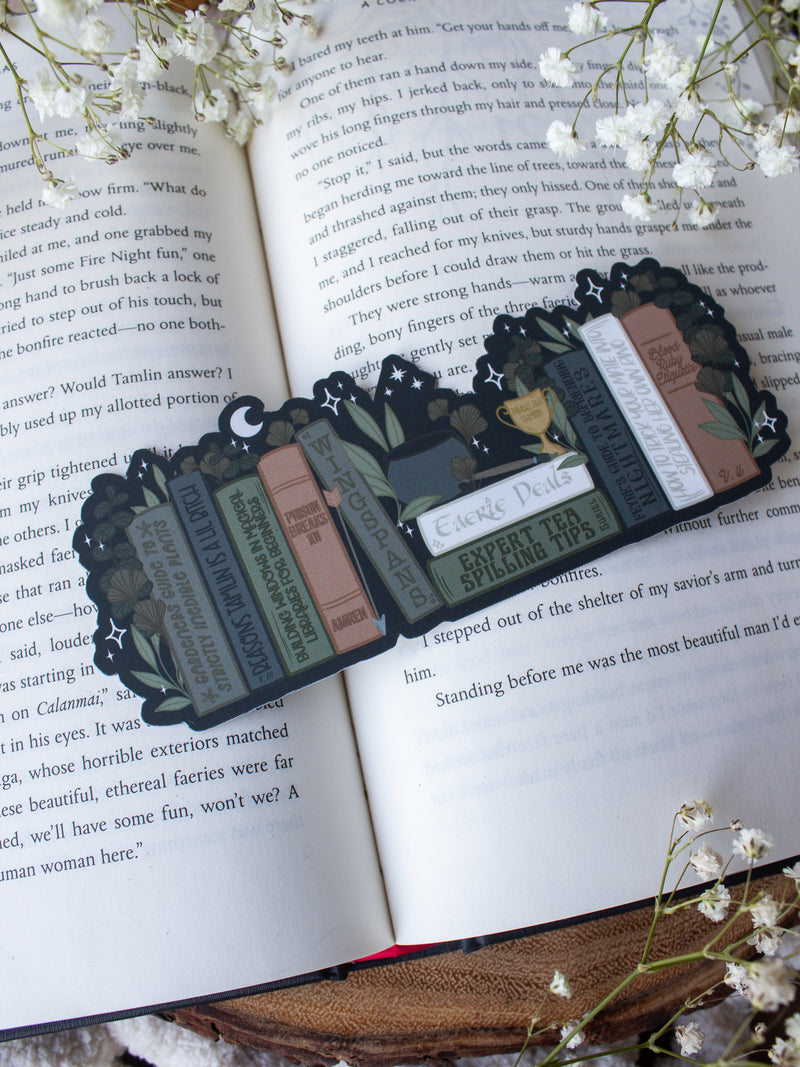 ACOTAR Funny Feyre Bookshelf Bookmark from A Court of Thorns and Roses by Sarah J Maas. A Bookshelf in earth tones like deep greens, browns and charcoal with a cauldron and a "snowball fight champion" trophy with book titles like "Reasons Tamlin is a lil bitch", "A Gardeners guide to strictly inedible plants", "Prison Breaks 101" and more.