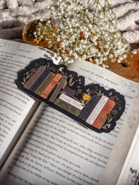 ACOTAR Funny Feyre Bookshelf Bookmark from A Court of Thorns and Roses by Sarah J Maas. A Bookshelf in earth tones like deep greens, browns and charcoal with a cauldron and a "snowball fight champion" trophy with book titles like "Reasons Tamlin is a lil bitch", "A Gardeners guide to strictly inedible plants", "Prison Breaks 101" and more.
