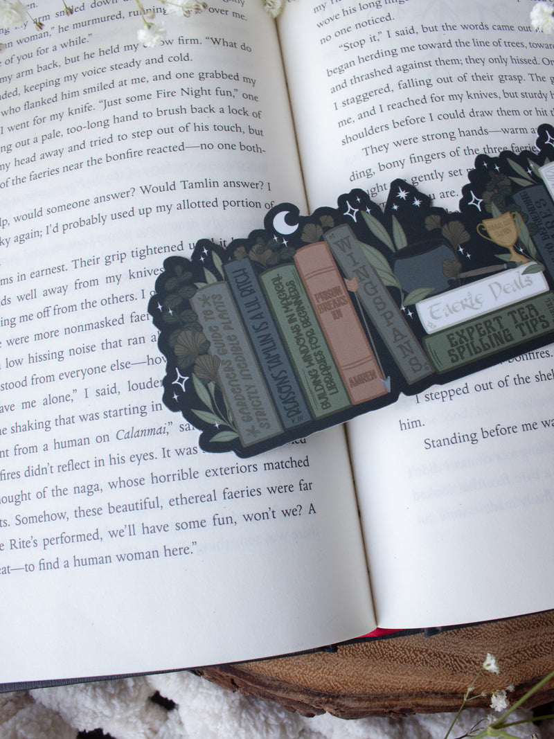 ACOTAR Funny Feyre Bookshelf Bookmark from A Court of Thorns and Roses by Sarah J Maas. A Bookshelf in earth tones like deep greens, browns and charcoal with a cauldron and a "snowball fight champion" trophy with book titles like "Reasons Tamlin is a lil bitch", "A Gardeners guide to strictly inedible plants", "Prison Breaks 101" and more.