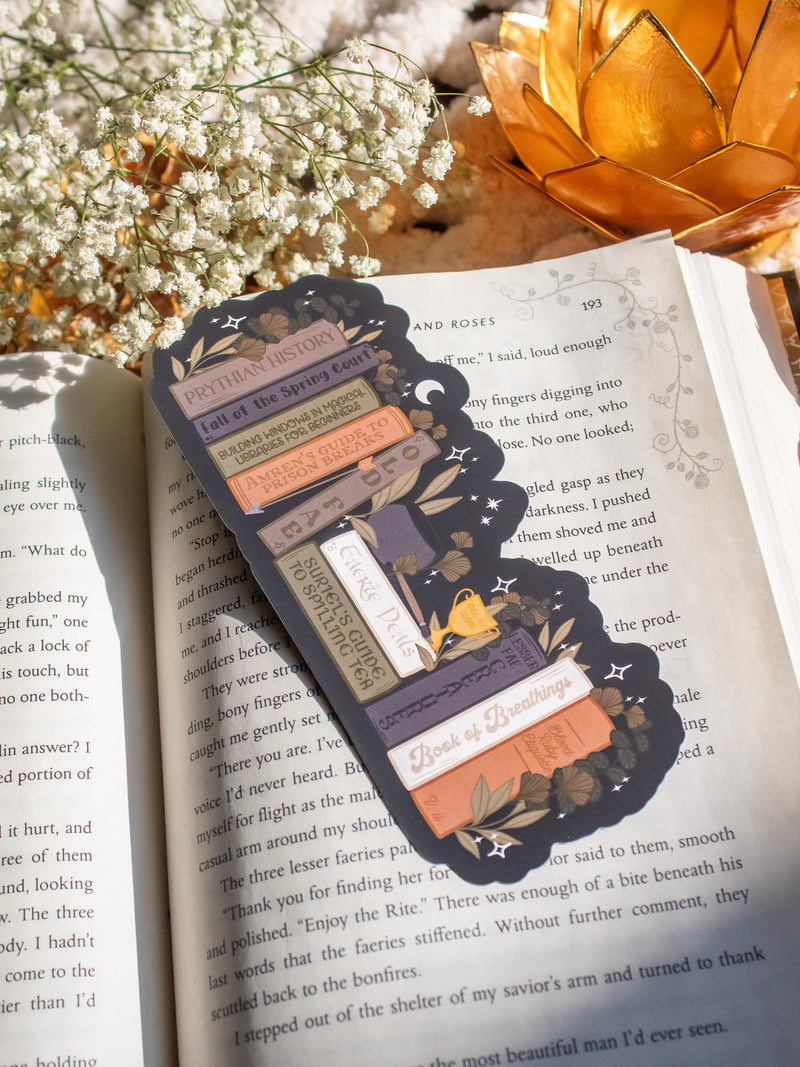 ACOTAR Funny Feyre Bookshelf Bookmark from A Court of Thorns and Roses by Sarah J Maas. A Bookshelf in earth tones like deep greens, browns and charcoal with a cauldron and a "snowball fight champion" trophy with book titles like "Reasons Tamlin is a lil bitch", "A Gardeners guide to strictly inedible plants", "Prison Breaks 101" and more.