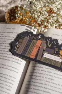 ACOTAR Funny Feyre Bookshelf Bookmark from A Court of Thorns and Roses by Sarah J Maas. A Bookshelf in earth tones like deep greens, browns and charcoal with a cauldron and a "snowball fight champion" trophy with book titles like "Reasons Tamlin is a lil bitch", "A Gardeners guide to strictly inedible plants", "Prison Breaks 101" and more.