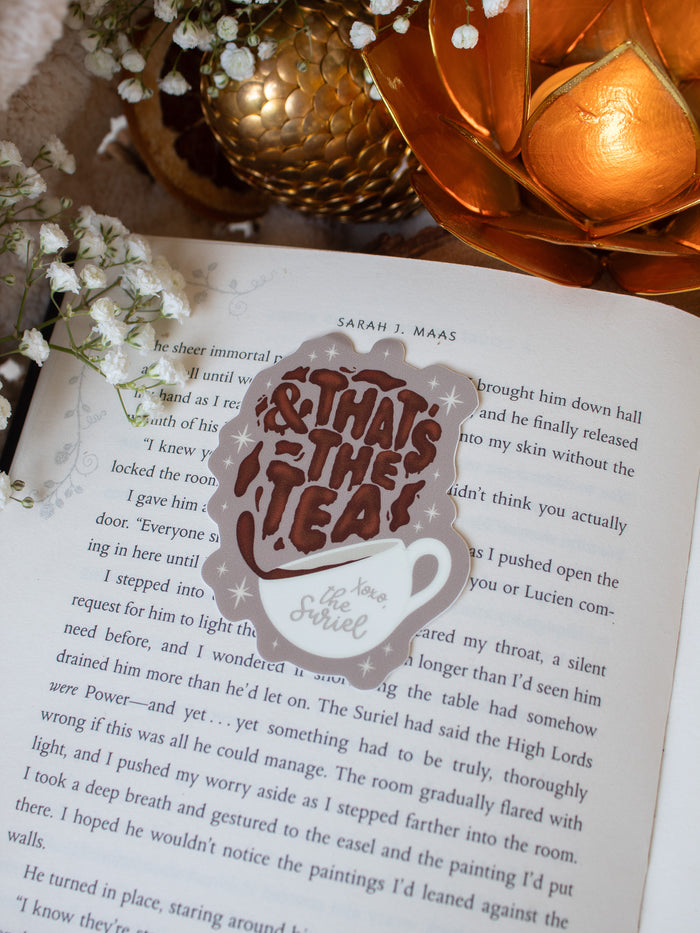 This ACOTAR Suriel Tea Co Teacup Sticker shows a teacup with tea splashing out of it, the tea makes the letters as it falls. 