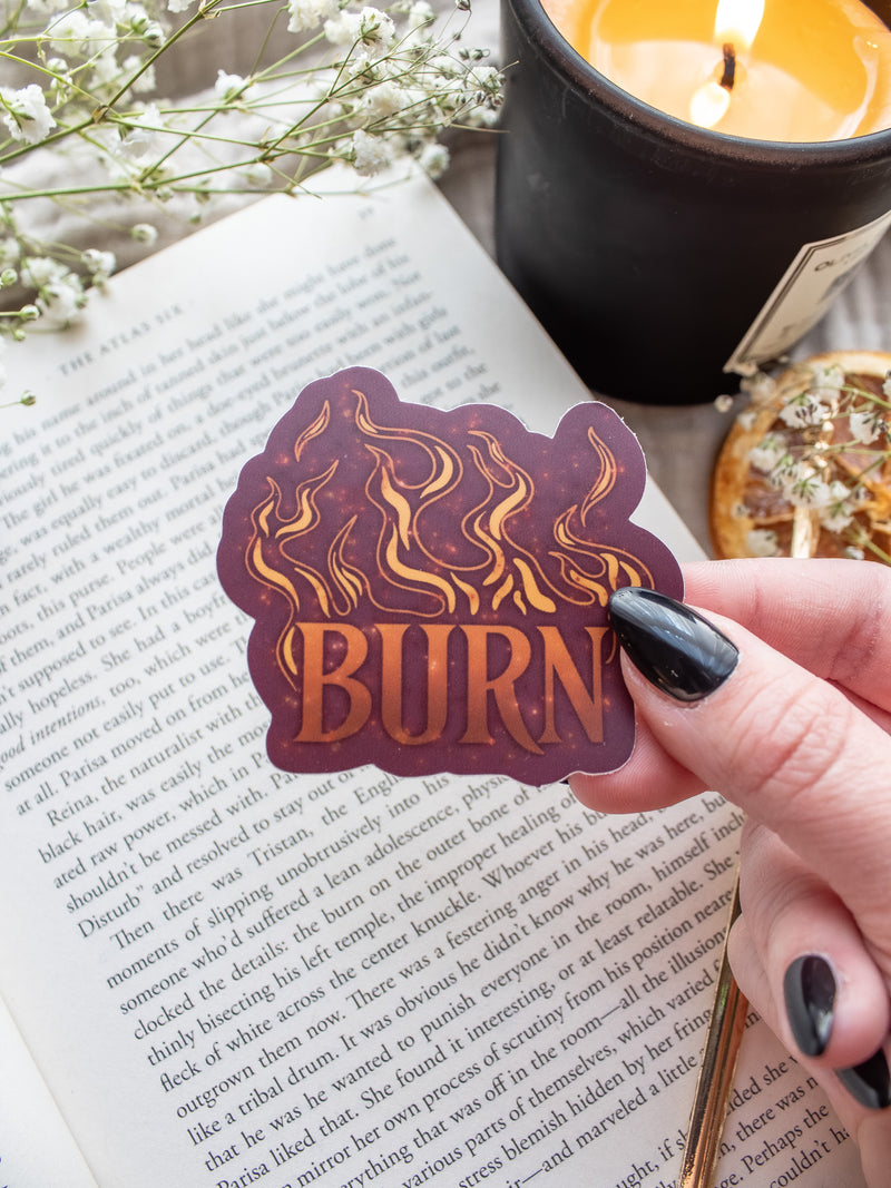 BURN Spark of The Everflame Vinyl Sticker from the Kindred's Curse Saga by Penn Cole. This licensed sticker is maroon with flames and BURN in big letters, with the colors looking like flames, little embers flying around. 