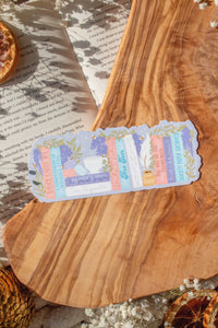 Bridgeton Inspired Die-Cut Bookmark for Regency Era Romance Readers. 

A regency era romance bookshelf design in light pinks, blues, violet, and ivory surrounded by wisteria on a lilac background. The bookmark is sitting on a wood cutting board, on an open book surrounded by little white flowers. 