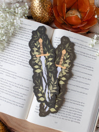 Broken Fantasy Sword Die-Cut Bookmark on an open book with a gold metal dragon egg, baby's breath, and an orange lotus tea light holder in the background. 
