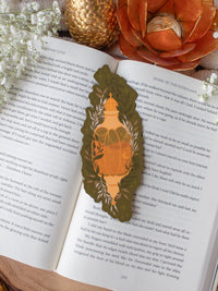 This fall autumn fantasy pumpkin spice potion bookmark features a pumpkin shaped potion bottle, in orange and yellow/gold on a deep green background with curling foliage, stars and magic bubbles surrounding it. 