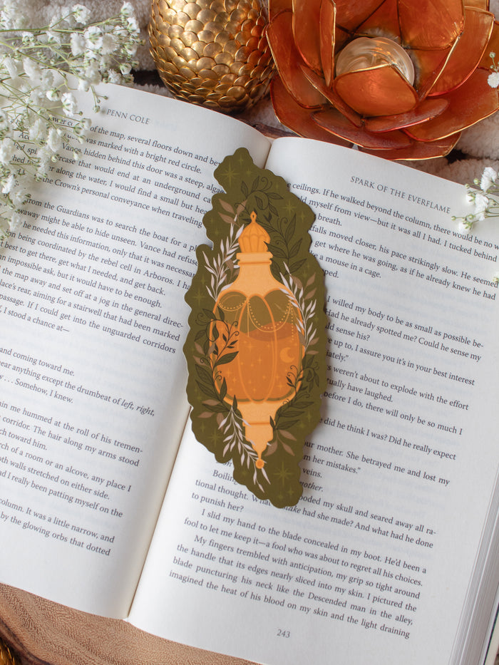 This fall autumn fantasy pumpkin spice potion bookmark features a pumpkin shaped potion bottle, in orange and yellow/gold on a deep green background with curling foliage, stars and magic bubbles surrounding it. 