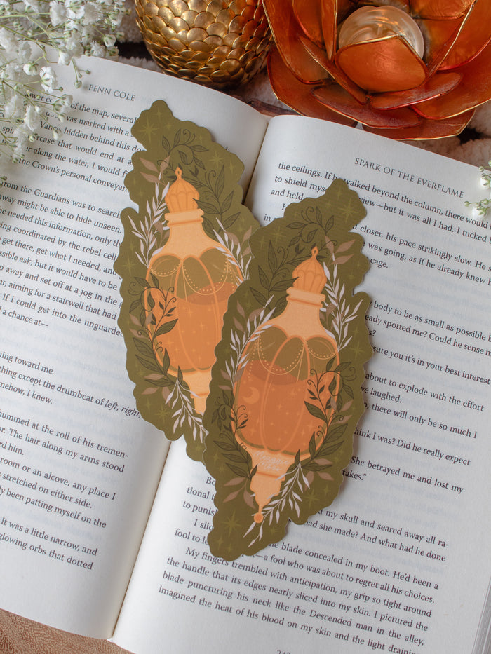 This fall autumn fantasy pumpkin spice potion bookmark features a pumpkin shaped potion bottle, in orange and yellow/gold on a deep green background with curling foliage, stars and magic bubbles surrounding it. 