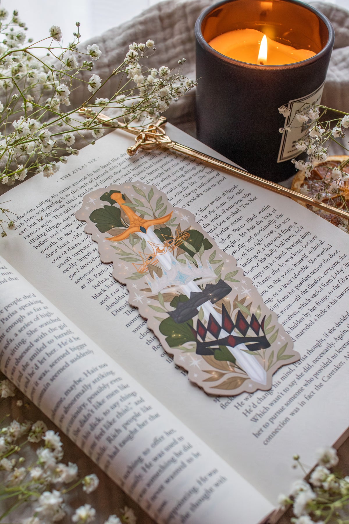 Inspired by Spark of the Everflame from the Kindreds Curse Saga by Penn Cole, this Crown Sword bookmark showcases crowns from four Emarion's realms. *Spoiler Alert, through Heat of the Everflame* - It shows all four crowns Diem has by the end of the 3rd book - Lumnos, Montios, Fortos, and Umbros.  All around a sword that is through the center of them, stacked one on top of the other. On a light beige background and surrounded by foliage, stars and lil magic light bubbles.