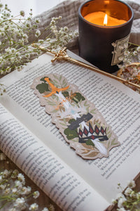 Inspired by Spark of the Everflame from the Kindreds Curse Saga by Penn Cole, this Crown Sword bookmark showcases crowns from four Emarion's realms. *Spoiler Alert, through Heat of the Everflame* - It shows all four crowns Diem has by the end of the 3rd book - Lumnos, Montios, Fortos, and Umbros.  All around a sword that is through the center of them, stacked one on top of the other. On a light beige background and surrounded by foliage, stars and lil magic light bubbles.