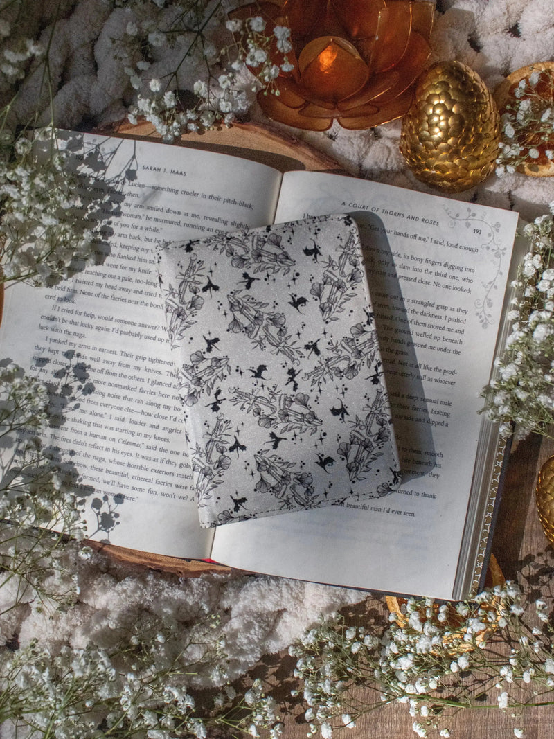 Ivory Swords Fantasy Reader Dragon Kindle Case. It has an ivory background with deep charcoal dragons, swords, crowns, and foliage all over it. This is a full cover kindle case with a leatherette outside, a kick-stand, card-slot, and hand-strap. 