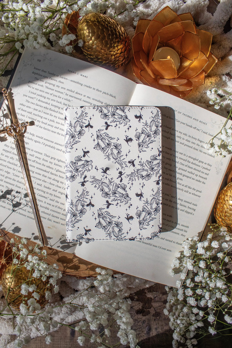 Ivory Swords Fantasy Reader Dragon Kindle Case. It has an ivory background with deep charcoal dragons, swords, crowns, and foliage all over it. This is a full cover kindle case with a leatherette outside, a kick-stand, card-slot, and hand-strap. 
