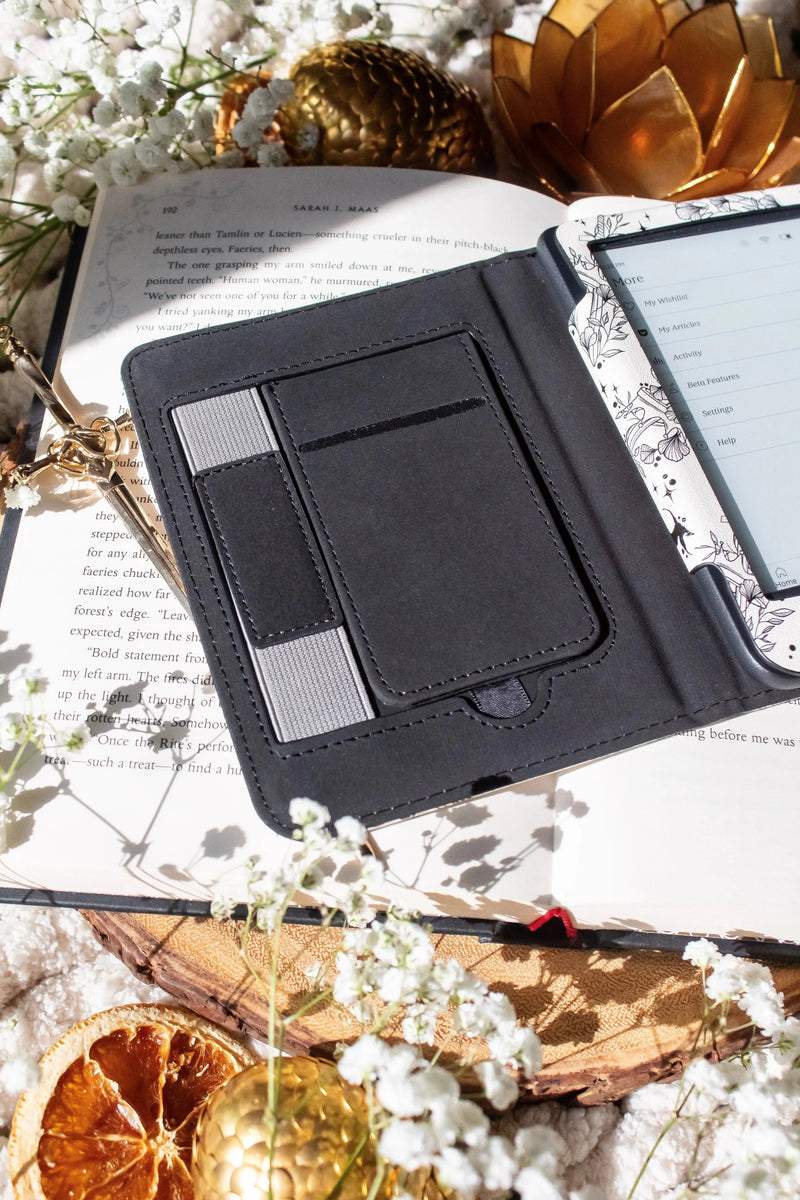 Ivory Swords Fantasy Reader Dragon Kindle Case. It has an ivory background with deep charcoal dragons, swords, crowns, and foliage all over it. This is a full cover kindle case with a leatherette outside, a kick-stand, card-slot, and hand-strap. 