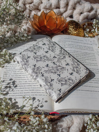 Ivory Swords Fantasy Reader Dragon Kindle Case. It has an ivory background with deep charcoal dragons, swords, crowns, and foliage all over it. This is a full cover kindle case with a leatherette outside, a kick-stand, card-slot, and hand-strap. 