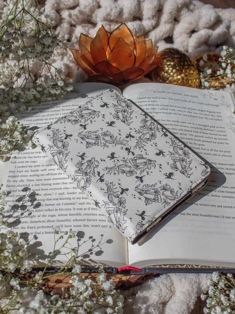 Ivory Swords Fantasy Reader Dragon Kindle Case. It has an ivory background with deep charcoal dragons, swords, crowns, and foliage all over it. This is a full cover kindle case with a leatherette outside, a kick-stand, card-slot, and hand-strap. 