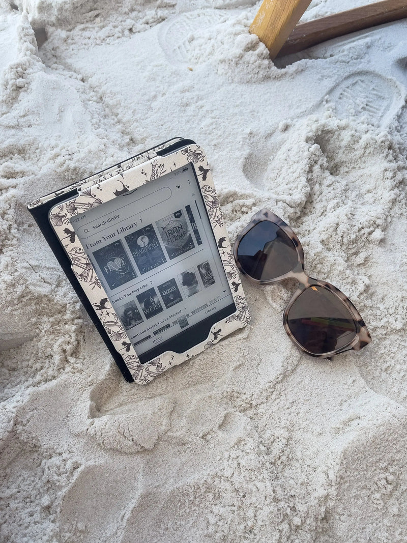 Ivory Swords Fantasy Reader Dragon Kindle Case. It has an ivory background with deep charcoal dragons, swords, crowns, and foliage all over it. This is a full cover kindle case with a leatherette outside, a kick-stand, card-slot, and hand-strap. 