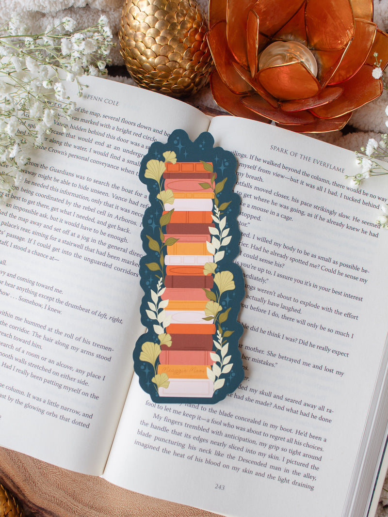 This moody toned fall autumn bookstack bookmark is a bookstack in warm tones, like mustard yellow, cream, coral, and burnt orange on a deep teal background. 