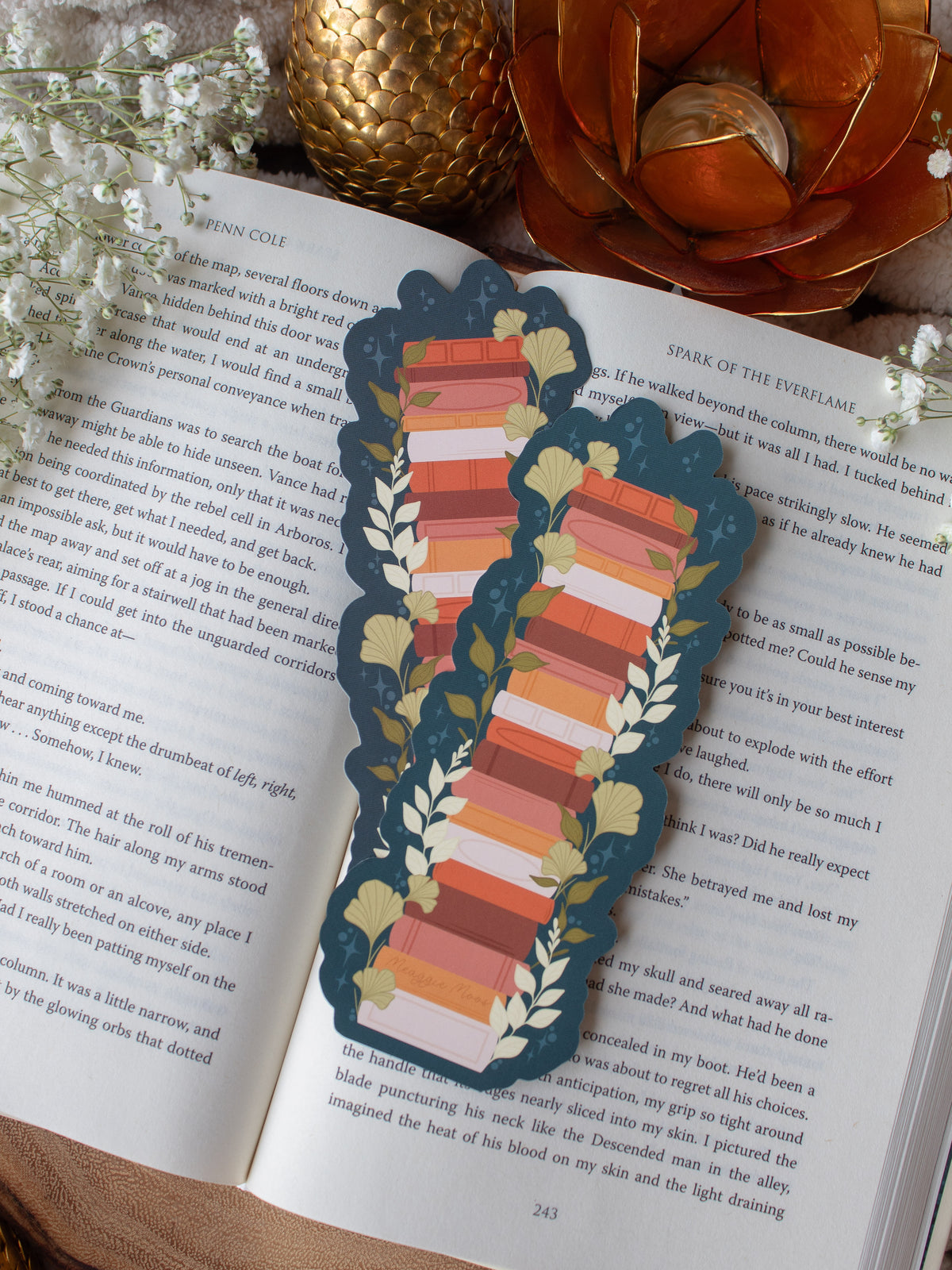 This moody toned fall autumn bookstack bookmark is a bookstack in warm tones, like mustard yellow, cream, coral, and burnt orange on a deep teal background. 