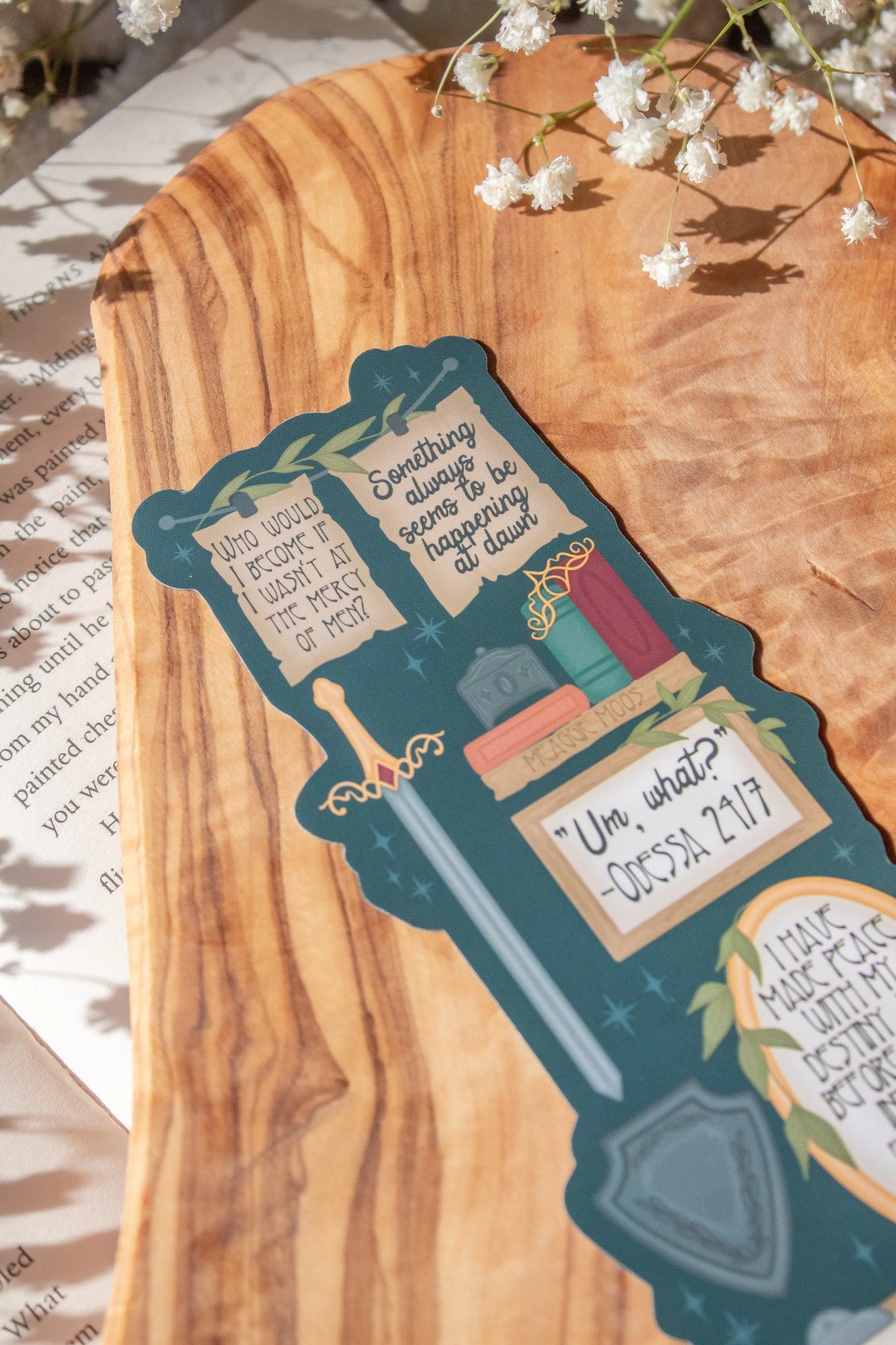 Bookmark inspired by the novel by Devney Perry. This bookmark is dark teal with frames on it with a bunch of different quotes from the book.

The bookmark is laid on an olive wood cutting board, sitting on an open book with little white flowers surrounding it.