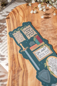 Bookmark inspired by the novel by Devney Perry. This bookmark is dark teal with frames on it with a bunch of different quotes from the book.

The bookmark is laid on an olive wood cutting board, sitting on an open book with little white flowers surrounding it.
