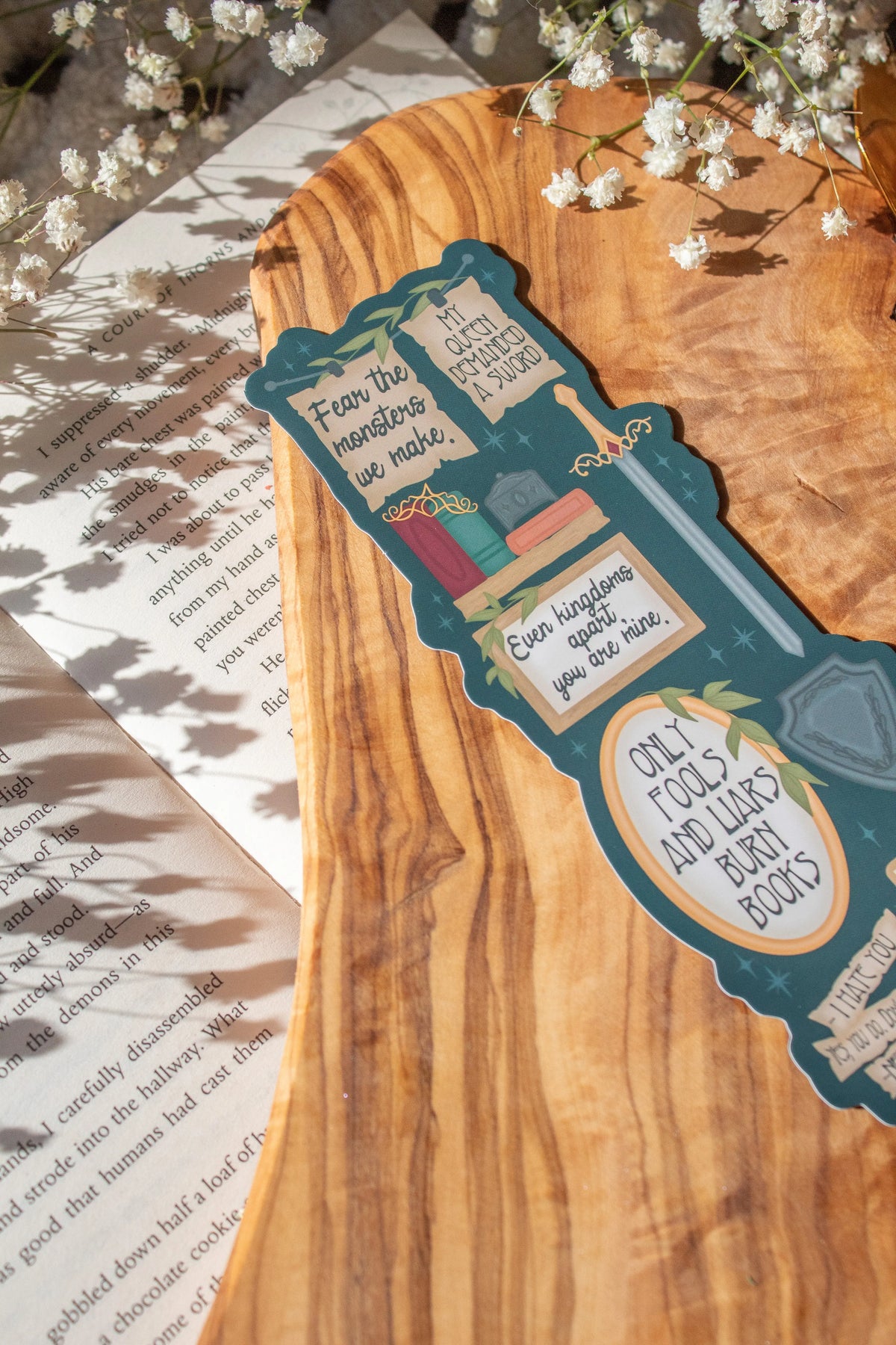 Bookmark inspired by the novel by Devney Perry. This bookmark is dark teal with frames on it with a bunch of different quotes from the book.

The bookmark is laid on an olive wood cutting board, sitting on an open book with little white flowers surrounding it.