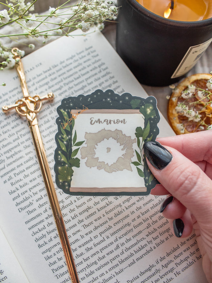 Spark of The Everflame Emarion Map Sticker. From The Kindred's Curse Saga by Penn Cole. This Licensed sticker has a dark green background with a banner showing a map of Emarion on it, with Diem's Lumnos crown hanging off the corner. 