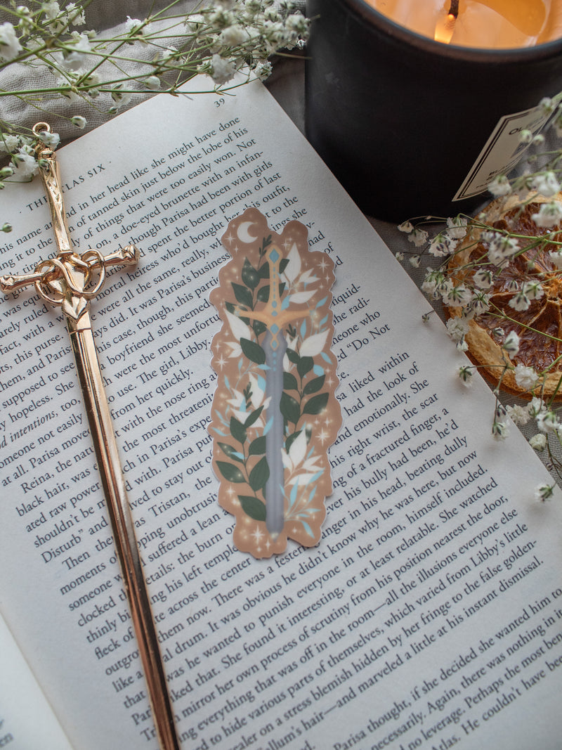Spark of the Everflame Sword of Corbois waterproof and dishwasher safe vinyl sticker. From the Kindred's Curse Saga by Penn Cole. This officially licensed sticker is a dark metal sword, surrounded by foliage, on a burn orange background. 