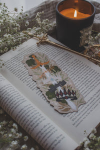Inspired by Spark of the Everflame from the Kindreds Curse Saga by Penn Cole, this Crown Sword bookmark showcases crowns from four Emarion's realms. *Spoiler Alert, through Heat of the Everflame* - It shows all four crowns Diem has by the end of the 3rd book - Lumnos, Montios, Fortos, and Umbros.  All around a sword that is through the center of them, stacked one on top of the other. On a light beige background and surrounded by foliage, stars and lil magic light bubbles.