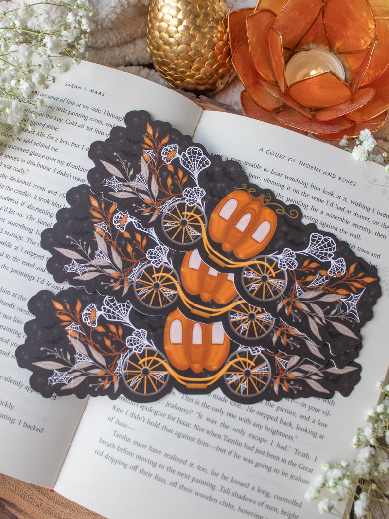 This spooky / halloween fairytale inspired midnight pumpkin carriage ride bookmark features a pumpkin shaped carriage with wheels off both sides. Surrounded by orange, tan, and white foliage that are covered in spider webs. 