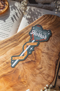 This Sucker for Horror Die-Cut Bookmark is for all my mystery loving book babes who love to delve into a good thriller. 

It is a dark grey heart shaped sucker with blood dripping off of it, wrapped in crime scene tape and surrounded by stars on a darker grey background.


The bookmark is sitting on an olive wood cutting board, on an open book, with little white flowers surrounding it.