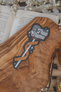 This Sucker for True Crime Die-Cut Bookmark is for all my mystery loving book babes who love to delve into a good cold case file. 

It is a dark grey heart shaped sucker with blood dripping off of it, wrapped in crime scene tape and surrounded by stars on a darker grey background.


The bookmark is sitting on an olive wood cutting board, on an open book, with little white flowers surrounding it.