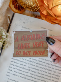 This "A Hushling Lives Here - Do Not Enter" sign sticker is inpsired by When the Moon Hatched by Sarah A Parker.  It features a wooden sign with bold red brushed text and little stars on the top left and bottom right side. It has a clear background.
