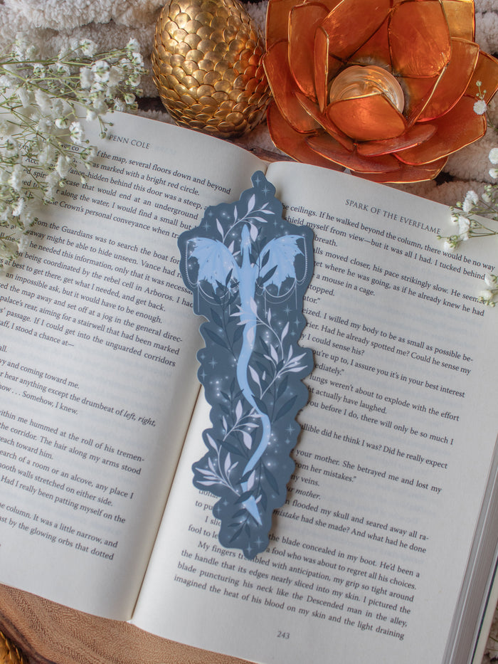 This When The Moon Hatched Moonplume Dragon Bookmark is from the Moonfall Series by Sarah A Parker. A light blue dragon is on a dust slate blue background with little magic bubbles