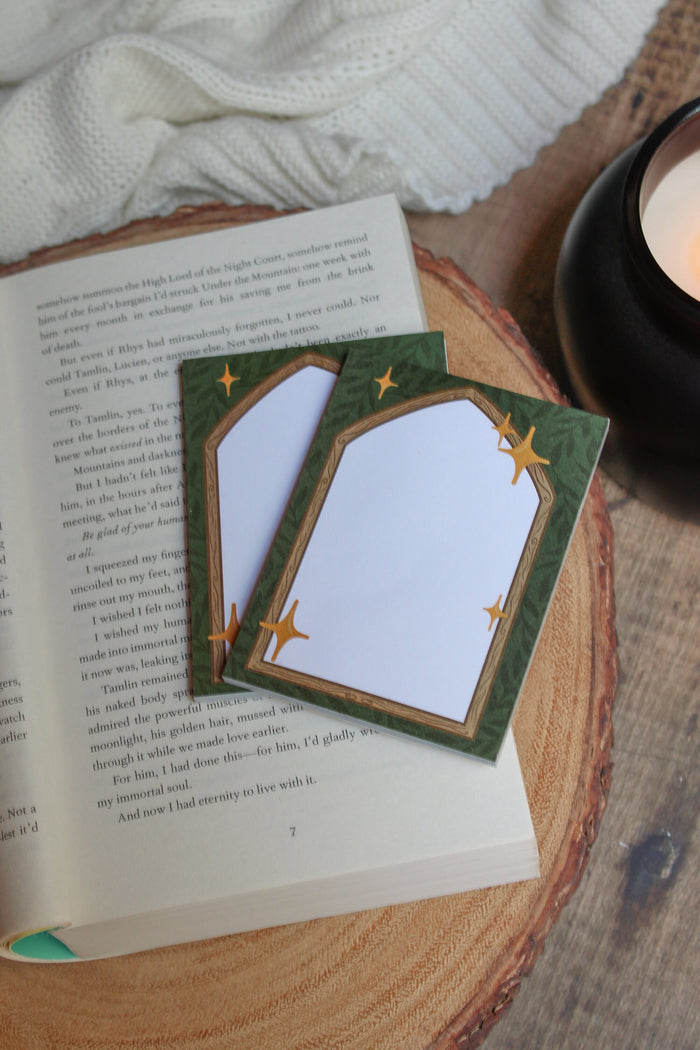 These Fantasy Bookish Archway Post-It Notepads have a dark green background with lil leaves on it. In front their is a wooden archway that comes to a point at the top. The center of the archway is solid write for the writing area. 
