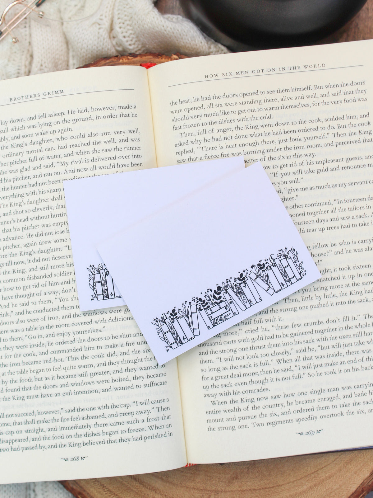 These bookish magical forest bookshelf post-it notepads are perfect to jot down all your bookish thoughts and ideas. They are 3"x4", have a white background with a black bookshelf along the bottom. The bookshelf have foliage peeking out from behind them. 