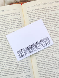 These bookish magical forest bookshelf post-it notepads are perfect to jot down all your bookish thoughts and ideas. They are 3"x4", have a white background with a black bookshelf along the bottom. The bookshelf have foliage peeking out from behind them. 