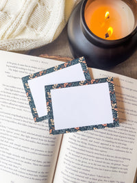 These floral faerie garden post-it notepads have a teal background with yellow and light sage green foliage and little orange celestial butterflies on them. Design is only around the border.